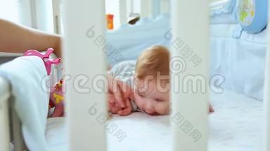 特写妈妈和一个小孩在婴儿床上玩，笑着从婴儿床的格子里看到侧面。 快乐的童年